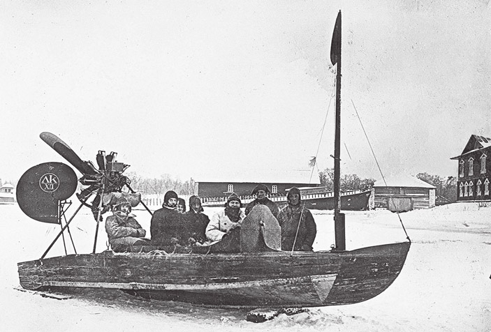 Архивная фотография: группа людей в аэросанях с воздушным винтом на заснеженной площади рядом с деревянными постройками
